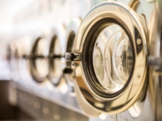  Close-up of a row of commercial washing machine doors in a laundromat, with the first chrome door open and the others receding in a blurred line.