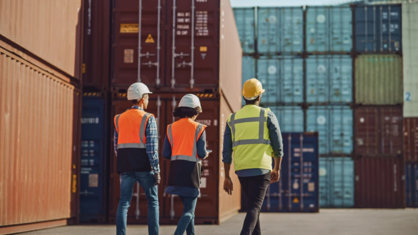 two men and woman walking in a shipping container yard image